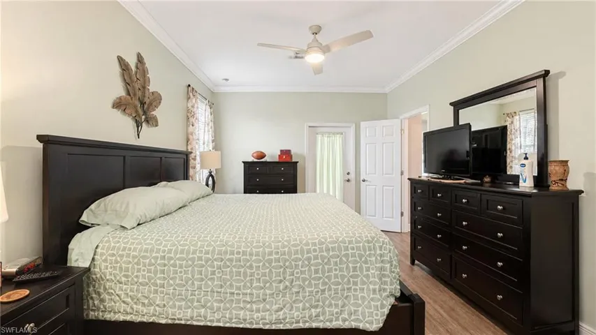 Spacious room featuring light green walls, crown molding, a ceiling fan with integrated lighting, wood-finish flooring, and a glass-paneled exterior door