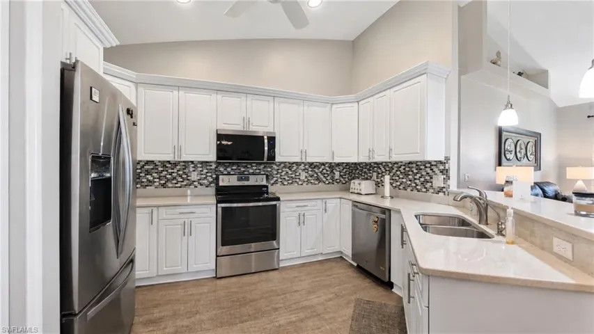 Modern kitchen featuring white cabinetry, stainless steel appliances, a mosaic tile backsplash, light-toned countertops, and wood-finish flooring