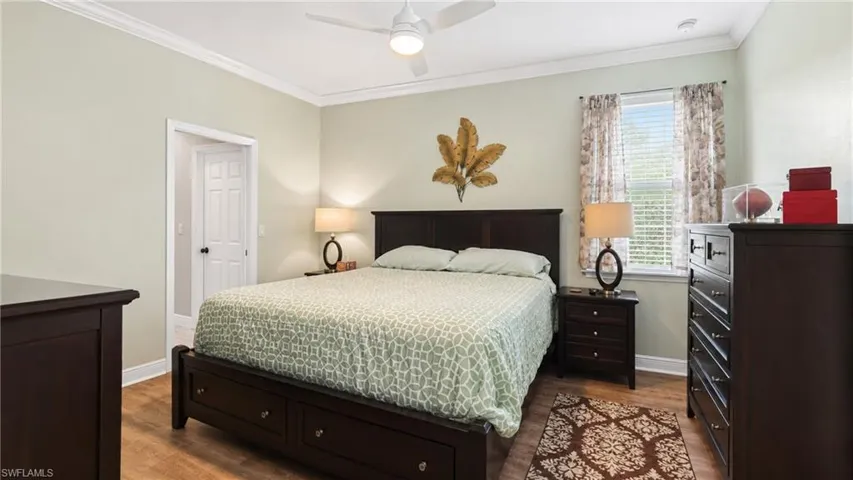 Bedroom featuring wood-finish flooring, a ceiling fan, crown molding, a window with blinds, and a white six-panel door