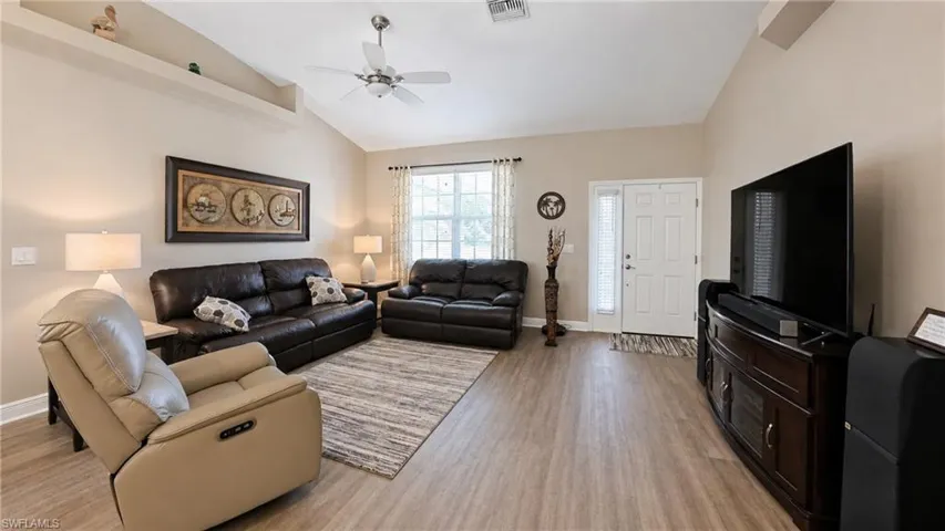 Spacious living area featuring vaulted ceilings, wood-finish flooring, a white paneled entry door with sidelight, and a ceiling fan with integrated lighting