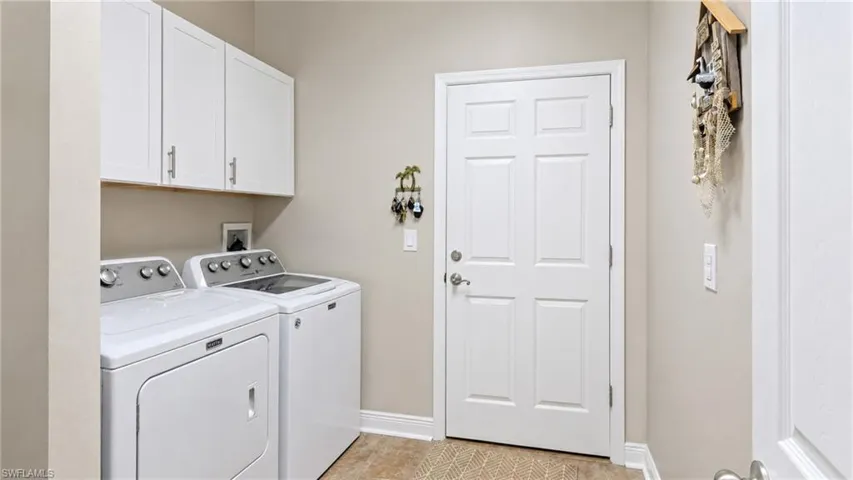 Dedicated utility space featuring overhead white shaker cabinetry with brushed nickel hardware, a durable tile-finish floor, and a paneled entry door