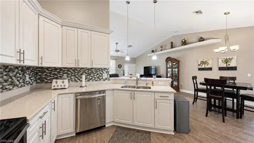 Kitchen featuring white cabinetry, light-toned countertops, mosaic tile backsplash, and stainless steel dishwasher