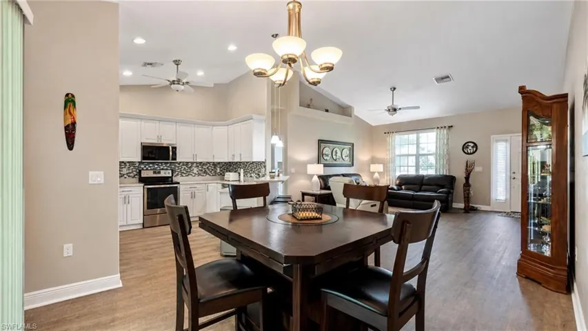 Open-concept living space featuring wood-finish flooring, a kitchen with white cabinetry and a mosaic tile backsplash, and a dining area with an overhead chandelier