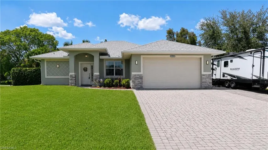 Exterior featuring a stone-accented facade, a paver driveway, a two-car garage, a covered entry, and a manicured lawn
