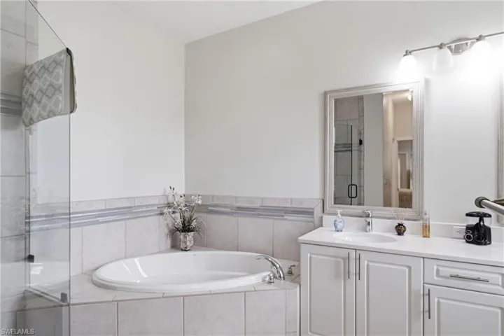 Bathroom with an integrated soaking tub, clear glass shower enclosure, and a vanity featuring a built-in sink and white cabinetry