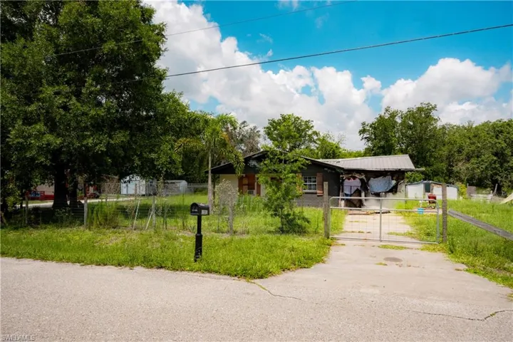 Single-story residence with a metal roof and light-colored siding, featuring a gated driveway and perimeter fencing