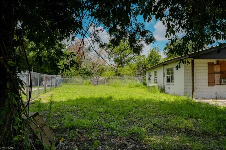 Expansive backyard featuring a chain-link fence, mature trees, and a white brick exterior