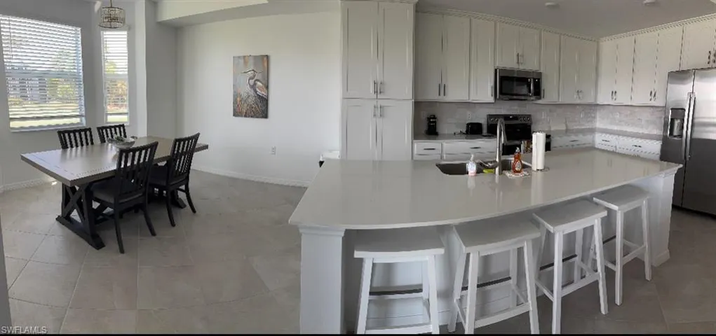 Kitchen with white cabinetry, appliances with stainless steel finishes, backsplash, light tile patterned floors, and a kitchen bar