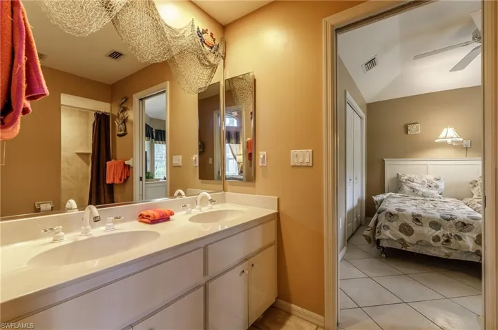 Full bathroom with double vanity, light tile patterned flooring, ceiling fan, and ensuite bath