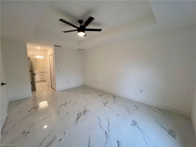 Primary bedroom with ceiling fan and a tray ceiling and entrance to ensuite bath and walk in closet.