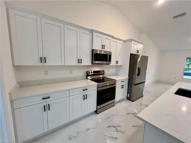 Kitchen featuring vaulted ceiling, appliances with stainless steel finishes, white cabinets, and light QUARTZ countertops.