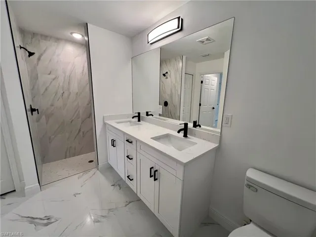 Primary bathroom featuring dual sinks vanity, toilet, and a tile shower.