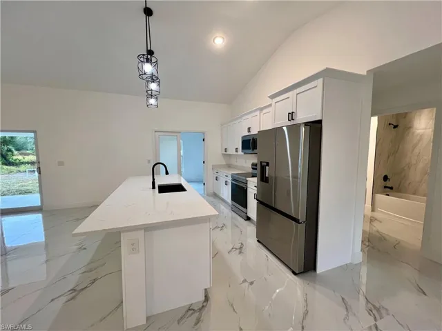 Kitchen featuring stainless steel appliances, a kitchen island with sink, hanging light fixtures, white cabinets, and sink with QUARTZ TOPS.