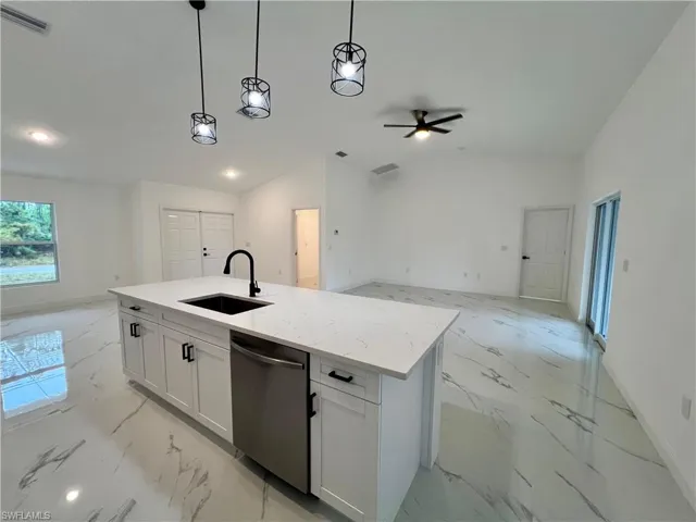 Kitchen with QUARTZ COUNTERTOPS a kitchen island with sink, lofted ceiling, stainless steel dishwasher, white cabinets, and sink