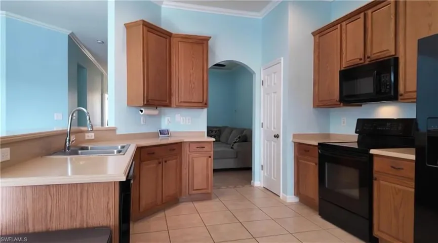 Kitchen with black appliances, arched walkways, light countertops, ornamental molding, and light tile patterned flooring