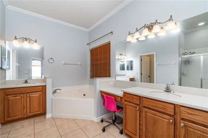 Bathroom with crown molding, two vanities, a bath, light tile patterned floors, and a stall shower