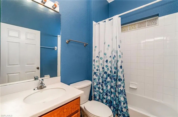 Bathroom with shower / bathtub combination with curtain, vanity, and a textured wall