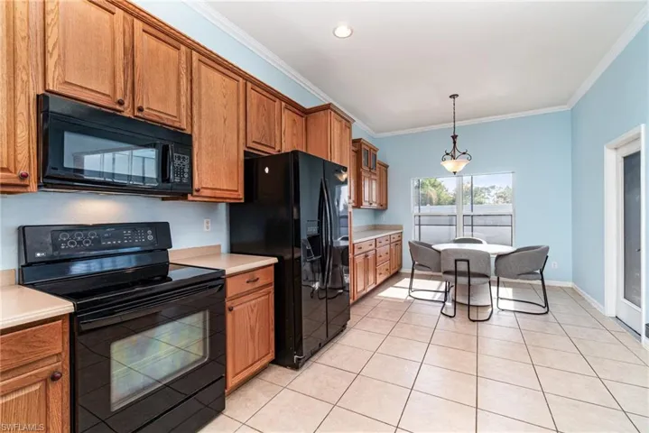Kitchen featuring black appliances, brown cabinets, light countertops, crown molding, and hanging light fixtures