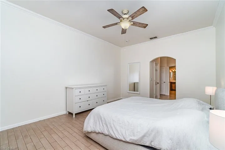 Bedroom featuring crown molding, wood finish floors, arched walkways, and a ceiling fan