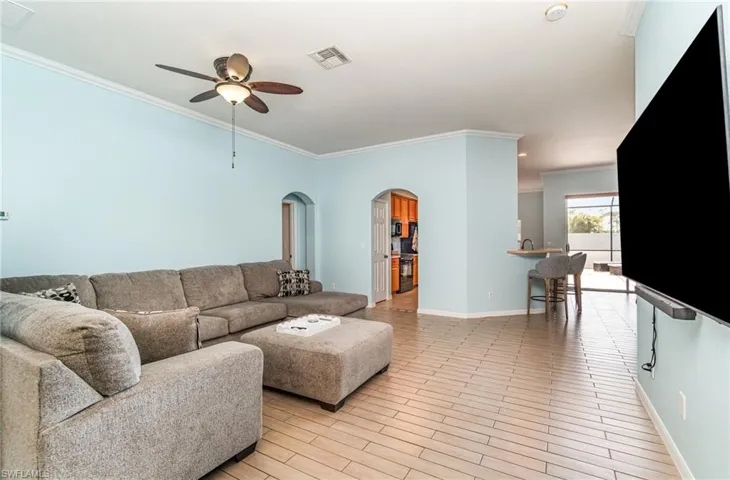 Living room with ornamental molding, arched walkways, wood finish floors, and ceiling fan