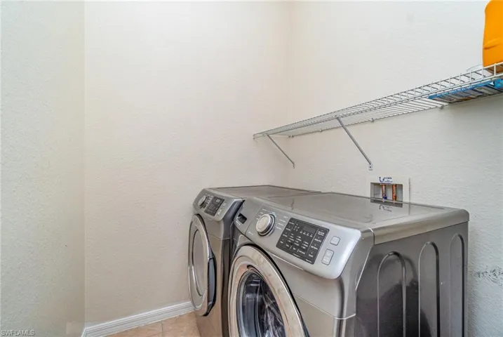 Washroom featuring a textured wall, washer and dryer, and light tile patterned flooring