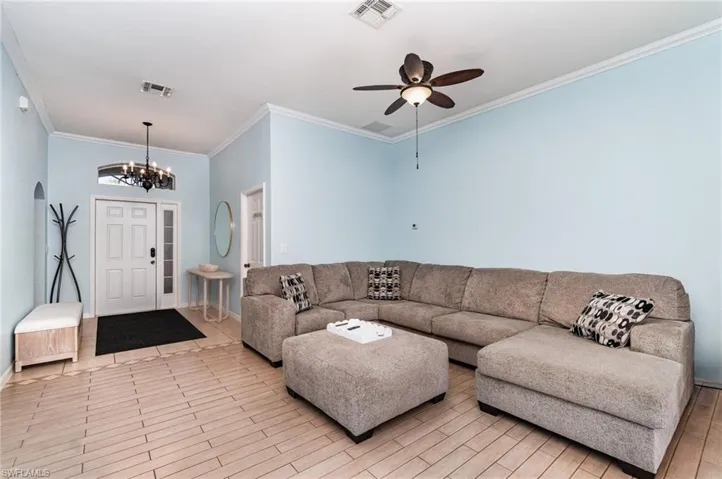 Living area featuring crown molding, a chandelier, ceiling fan, wood finish floors, and arched walkways