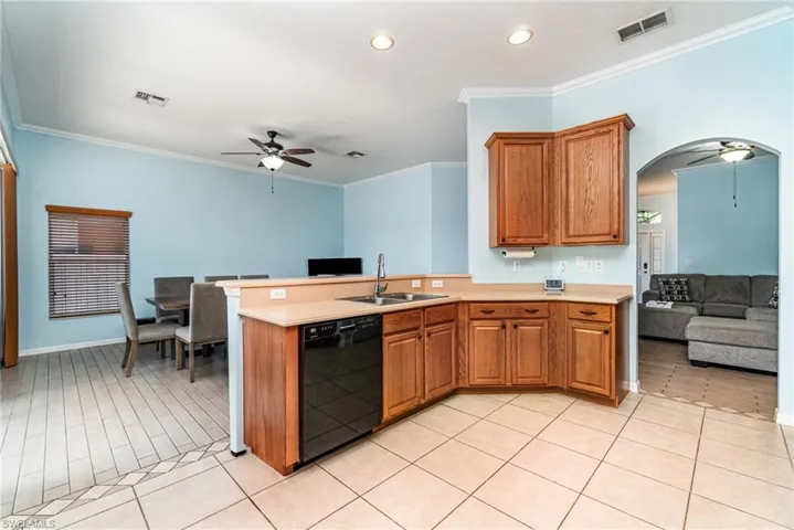 Kitchen with a ceiling fan, ornamental molding, brown cabinets, dishwasher, and arched walkways