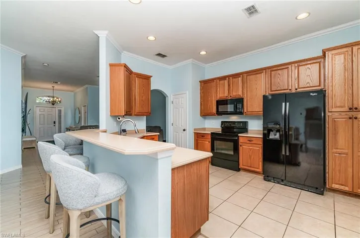 Kitchen featuring black appliances, crown molding, a peninsula, arched walkways, and light countertops