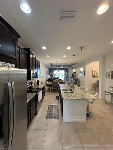 Kitchen featuring stainless steel appliances, light stone counters, open floor plan, a breakfast bar area, and a center island with sink
