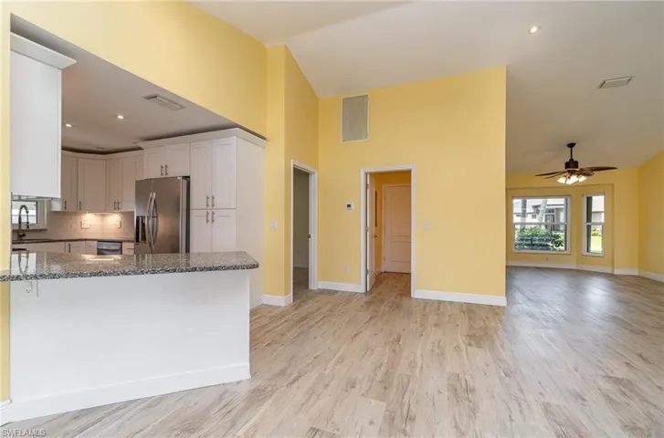Kitchen with light hardwood / wood-style floors, stainless steel appliances, stone countertops, backsplash, and white cabinets