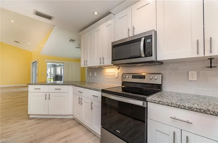 Kitchen with stone countertops, light hardwood / wood-style flooring, appliances with stainless steel finishes, white cabinets, and tasteful backsplash