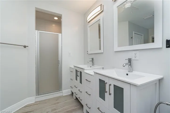 Primary bathroom featuring ceiling fan, an enclosed shower, dual vanity, and hardwood / wood-style flooring