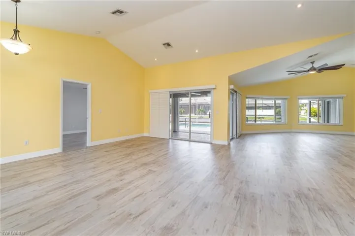 Unfurnished sitting area and living room with light hardwood / wood-style floors, plantation shutters on sliding windows, ceiling fan, and vaulted ceiling