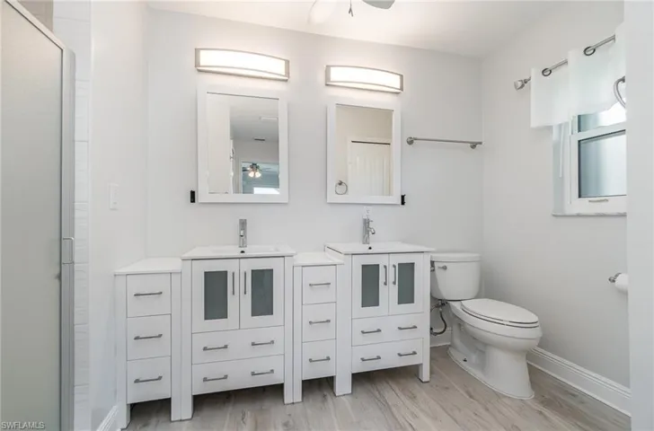 Primary bathroom featuring wood-type flooring, ceiling fan, dual vanity, and toilet