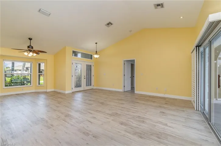 Unfurnished sitting area and dining area with high vaulted ceiling, ceiling fan, French door front entry, and light wood-type flooring