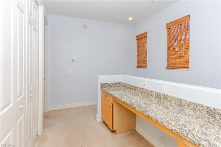 Built-in cabinetry with stone-finish countertop, dual windows with bamboo-style blinds, and double-door closet