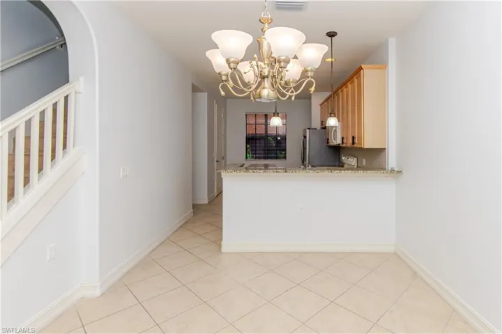 Interior space featuring ceramic tile flooring, a multi-arm chandelier with frosted glass shades, a breakfast bar with a stone-surface countertop, and wooden cabinetry
