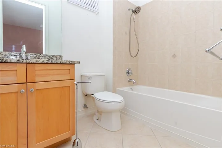 Bathroom featuring light wood-finish cabinetry, a stone-pattern countertop, an undermount sink, and a tiled shower-tub combination with a handheld sprayer