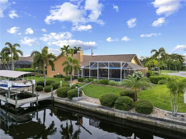 Rear view of property featuring a lanai, a water view, boat lift, and a lawn