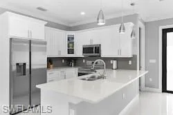 Kitchen featuring stainless steel appliances, glass insert cabinets, hanging light fixtures, crown molding, and white cabinets