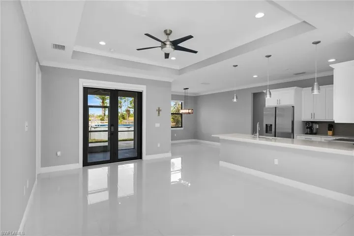 Unfurnished living room with a tray ceiling, a ceiling fan, crown molding, recessed lighting, and french doors
