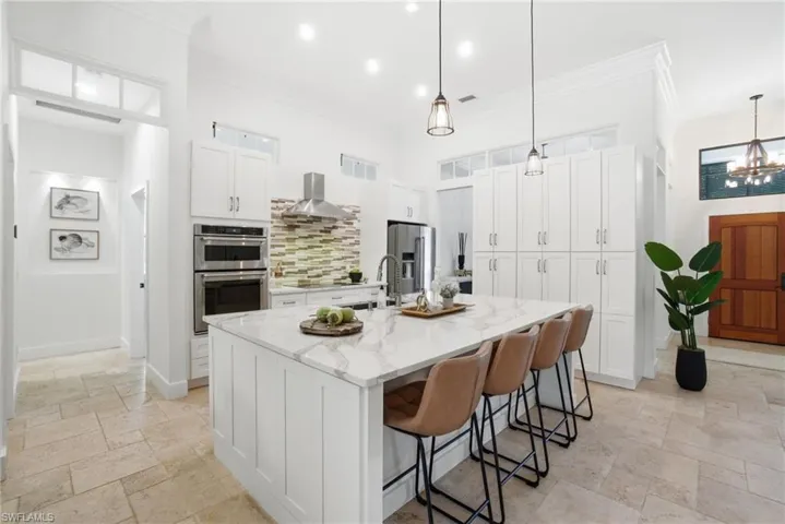 Kitchen featuring white cabinets, stone tile flooring, a breakfast bar, a center island with sink, and stainless steel appliances