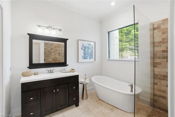 Full bathroom featuring vanity, ornamental molding, a freestanding bathtub, and a step free walk in shower