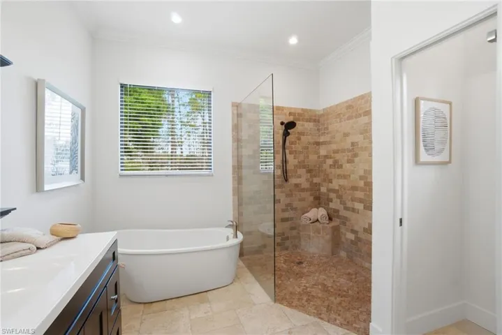 Full bathroom featuring vanity, ornamental molding, a freestanding bathtub, and a step free walk in shower