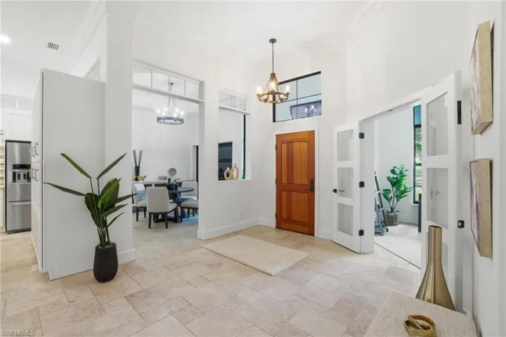 Foyer entrance featuring a high ceiling, stone tile floors, crown molding, and hanging lights