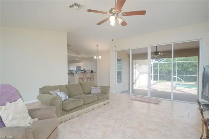 Tiled living room with ceiling fan with notable chandelier and vaulted ceiling