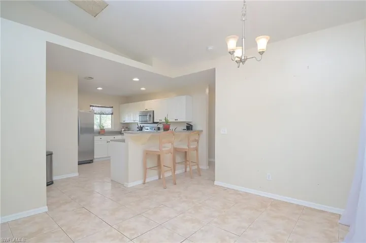 Kitchen featuring kitchen peninsula, stainless steel appliances, a kitchen bar, white cabinetry, and light tile floors