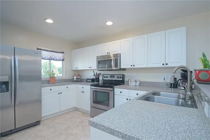 Kitchen with white cabinetry, stainless steel appliances, light tile flooring, and sink