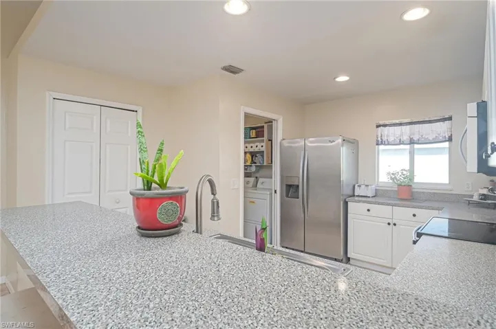 Kitchen featuring stainless steel refrigerator with ice dispenser, range, light stone countertops, washer and dryer, and white cabinets