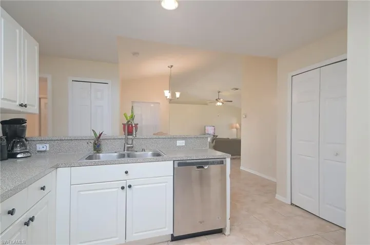 Kitchen featuring decorative light fixtures, stainless steel dishwasher, white cabinets, sink, and light tile floors